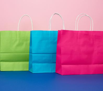 multicolored paper bags for shopping and gifts with white handles stand on a pink-blue background