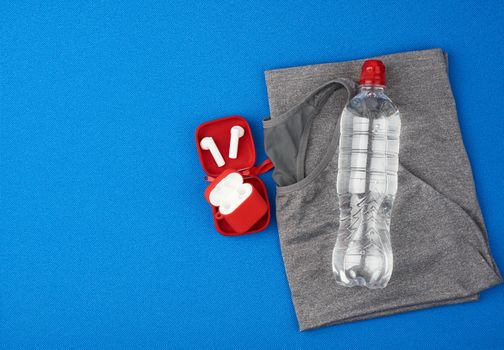 folded gray sports female T-shirt and water bottle on a blue background, set for sports and yoga