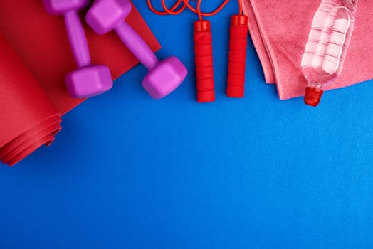 pair of purple plastic dumbbells, bottle of water  on a red neoprene mat, top view, training equipment