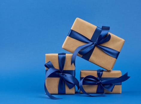 rectangle box wrapped in brown kraft paper and tied with a silk blue ribbon, gift on a dark blue background, copy space
