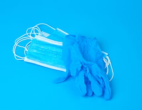 disposable gloves and stack of medical masks made of non-woven material with white rubber bands on a blue background, protective accessory for the respiratory tract from the virus