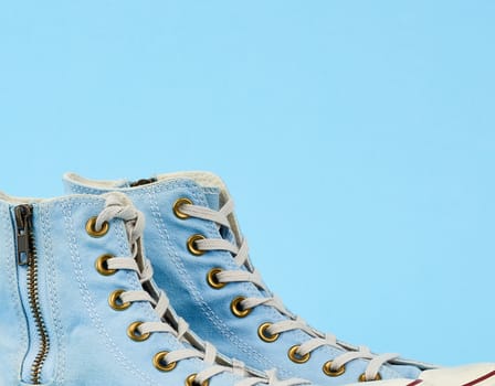 fragment of a pair of light blue worn textile sneakers with laces and zippers on a blue background, side view of shoes, close up