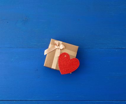 closed golden cardboard box with a gift and red paper heart, blue wooden background from boards, top view