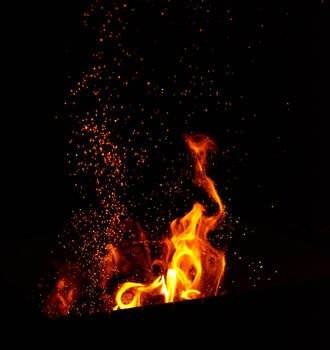 large burning bonfire with flame and orange sparks that fly in different directions on a black background