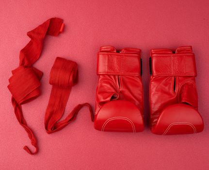 pair of red leather boxing gloves and a textile red elastic bandage for hands lie on a neoprene mat, sports set