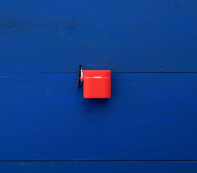 white wireless headphones, charging box and red silicone case on a blue wooden background, top view