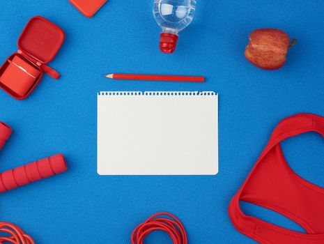 red sports shirt, red jump rope and wireless headphones in a red case on a blue background, top view, in the middle of an empty white sheet of paper, flat lay