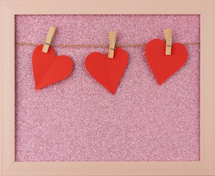 carved red paper hearts hanging on a brown rope, pink shiny background, valentines day card
