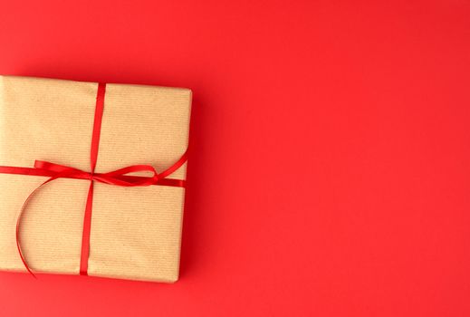 box wrapped in brown kraft paper and tied with a red thin silk ribbon on a red background, holiday Valentine's Day.  Anniversary, birthday.