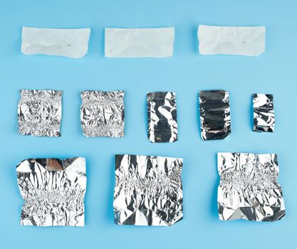 various crumpled white paper and foil used candy wrappers on a blue background, top view