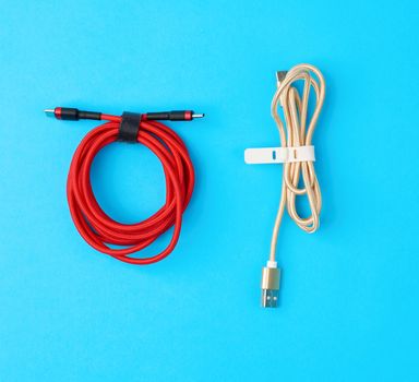 twisted cable for charging mobile devices in a red and golden textile wrapper on a blue background