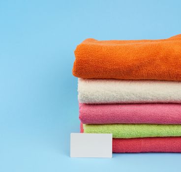 stack of multi-colored terry towels to wipe the body after a shower and a white blank paper business card on a blue background