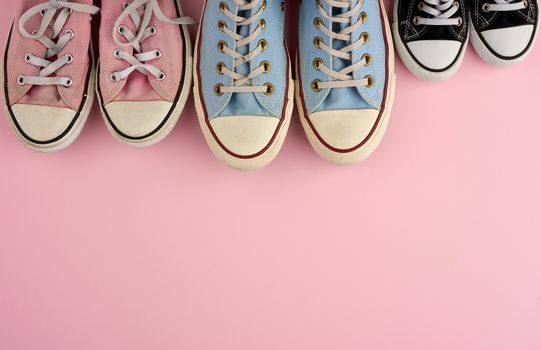 many multi-colored well-worn textile sneakers of different sizes on a pink background, top view, concept, family and team, friendship, copy space