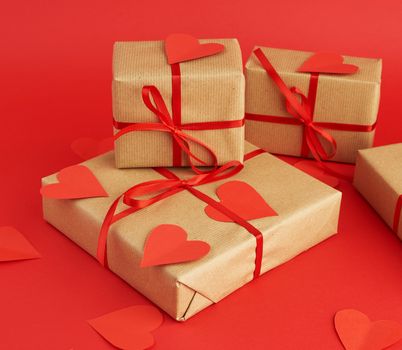 box wrapped in brown kraft paper and tied with a red thin silk ribbon, cut out of paper hearts, red background, gift for Valentine's Day, birthday