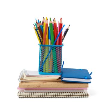 wooden multi-colored pencils, plastic pens and a stack of paper notebooks are isolated on a white background, stationery