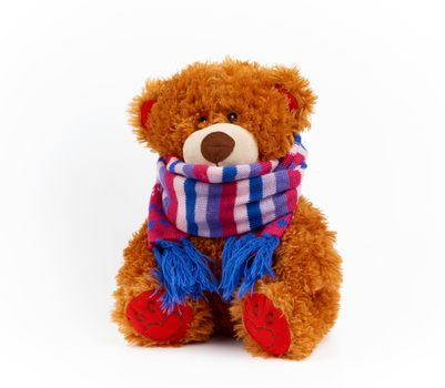 cute brown teddy bear in a colored knitted scarf sitting on a white background, concept of colds in children