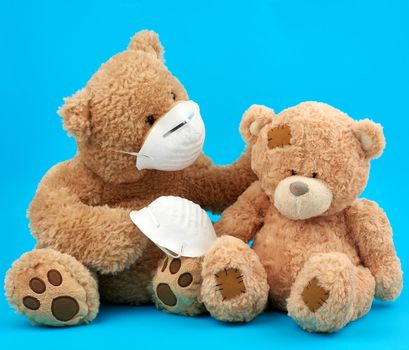 large teddy bear in a white mask transfers the accessory to another, concern for the health of those who are exposing, toys on a blue background
