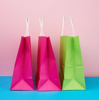 empty multicolored paper bags for shopping and gifts with white handles stand on a pink-blue background, copy space