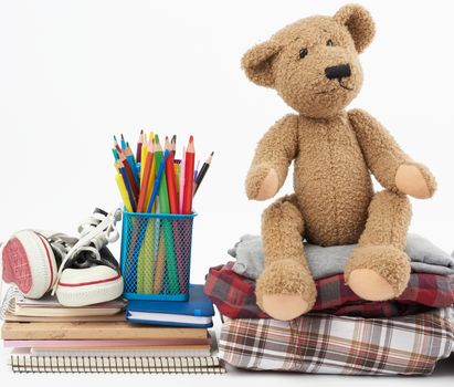 stack of folded clothes, sports sneakers, stationery and a brown teddy bear on a white background, concept for helping the needy, donation