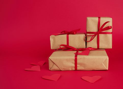 stack of wrapped gifts in brown kraft paper and tied with a red ribbon on a red background, surprise and a gift for Valentine's Day February 14