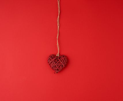 red wicker decorative heart hanging on brown rope, red festive background for Valentine's day