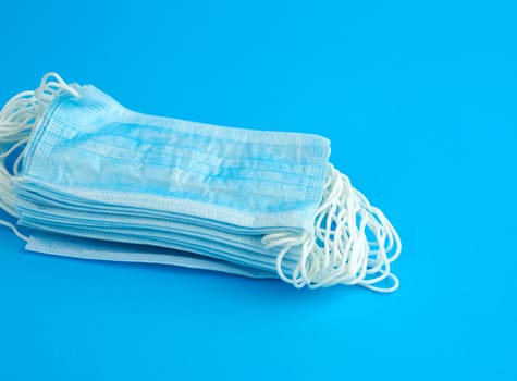 stack of medical masks made of non-woven material with white rubber bands on a blue background, protective accessory for the respiratory tract from the virus, top view