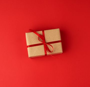 box wrapped in brown kraft paper and tied with a red thin silk ribbon on a red background, holiday Valentine's Day. Anniversary, birthday