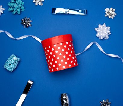closed cardboard red box with white polka dots and red silk ribbon on a blue background, holiday backdrop