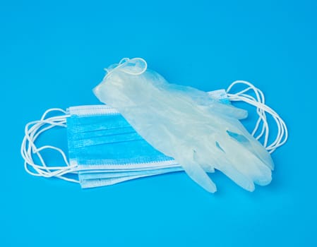 disposable gloves and stack of medical masks made of non-woven material with white rubber bands on a blue background, protective accessory for the respiratory tract from the virus