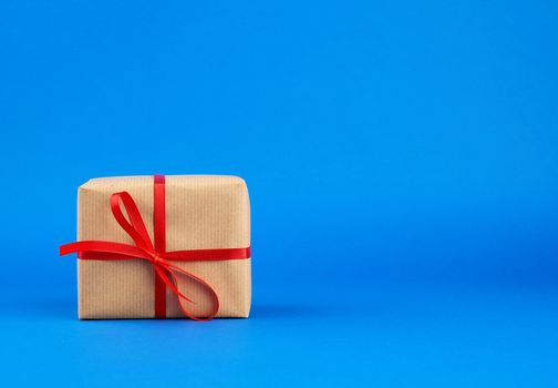 box wrapped in brown paper and tied with a red bow, gift on a blue background. Great design for any purposes. Holiday background. Valentine gift.