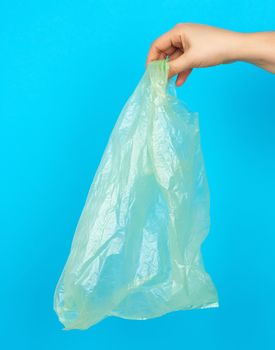 hand holds an empty green plastic bag on a blue background, concept of rejection of plastic and the transition to eco-packaging