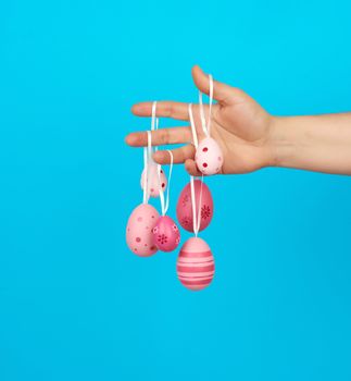 female hand holds easter colored pink eggs on a rope, blue background