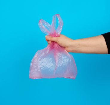 hand holds an empty pink plastic bag on a blue background, concept of rejection of plastic and the transition to eco-packaging