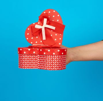 hand holds a red heart-shaped cardboard box with silk ribbon on a blue background, gift giving concept