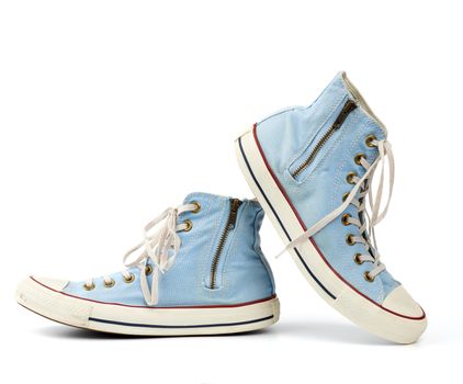 pair of light blue worn textile sneakers with laces and zippers on a white background, side view of shoes