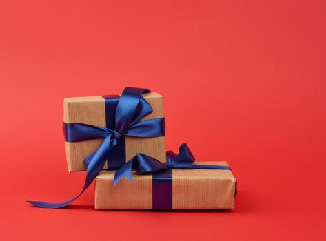 stack of gifts wrapped in brown kraft paper and a silk blue ribbon, red background. festive backdrop for birthday and valentines day