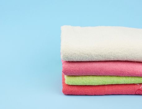 stack of colored cotton terry folded towels on a blue background, copy space