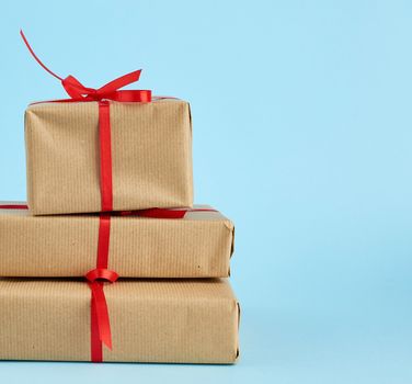 stack of boxes wrapped in brown paper and tied with a red bow, gifts on a blue background, copy space