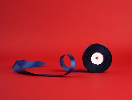 spool of twisted dark blue silk shiny ribbon on a red background, festive design element