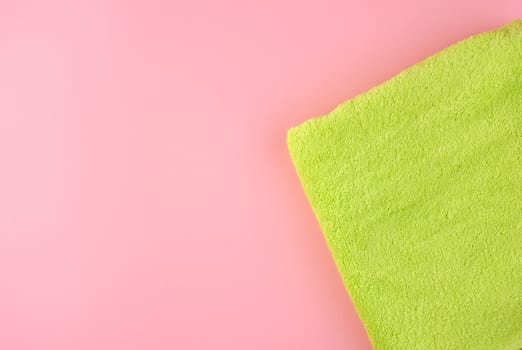 green cotton terry towel folded on a pink background, top view, copy space
