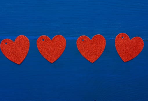 paper red shiny decorative hearts on dark blue wooden background, abstract festive backdrop for valentines day february 14