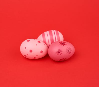 three colored pink easter eggs on a red background, close up