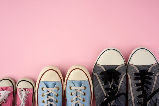 lot of textile worn sneakers of different sizes on a pink background, empty space, family concept