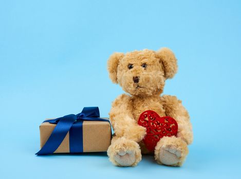 cute little brown teddy bear holds a brown box with a blue ribbon on a blue background
