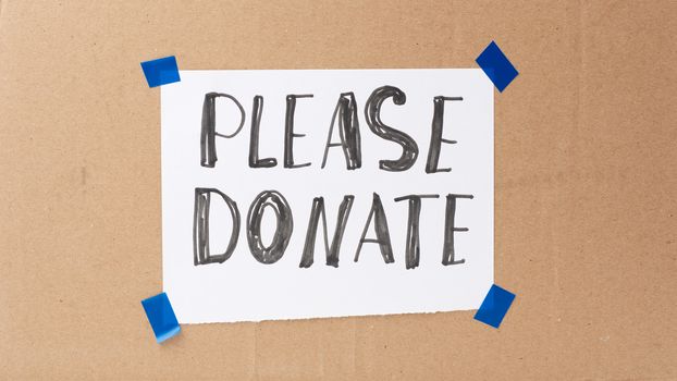 inscription please donate on a white sheet and glued brown cardboard paper, concept of volunteering and promotion