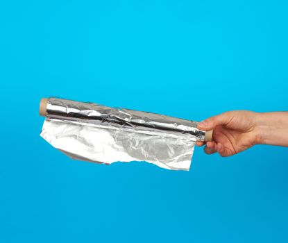hand holds a roll with twisted gray shiny foil on a blue background, food packaging