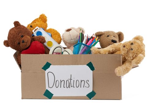 brown cardboard box filled with soft toys, school supplies isolated on white background, concept of charity and help to needy children