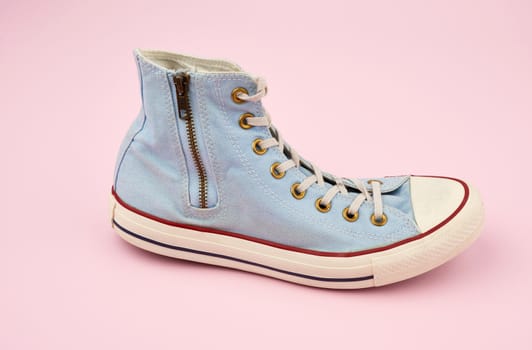 light blue worn textile sneaker with laces and zippers on a pink background, side view of shoes