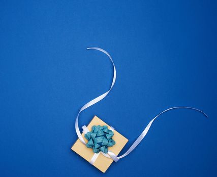 brown square box with a gift tied with a white ribbon with a bow on a blue classic background, top view, empty place for an inscription