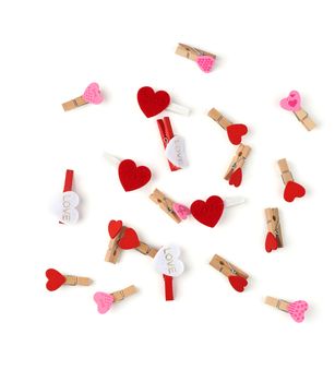 wooden decorative clothespins scattered on a white background with red hearts, top view